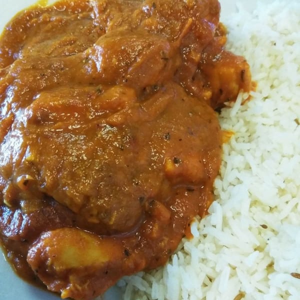 Close-up of Indian chicken curry with a rich orange sauce, served alongside fluffy white rice.