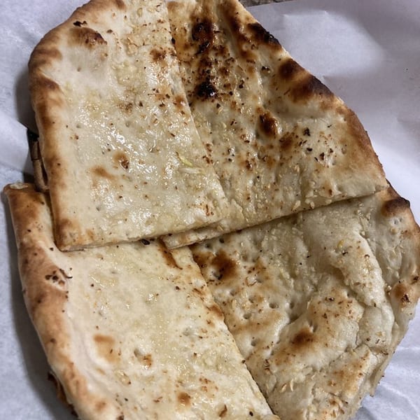 Close-up of several pieces of golden-brown naan bread, lightly charred and sprinkled with herbs.