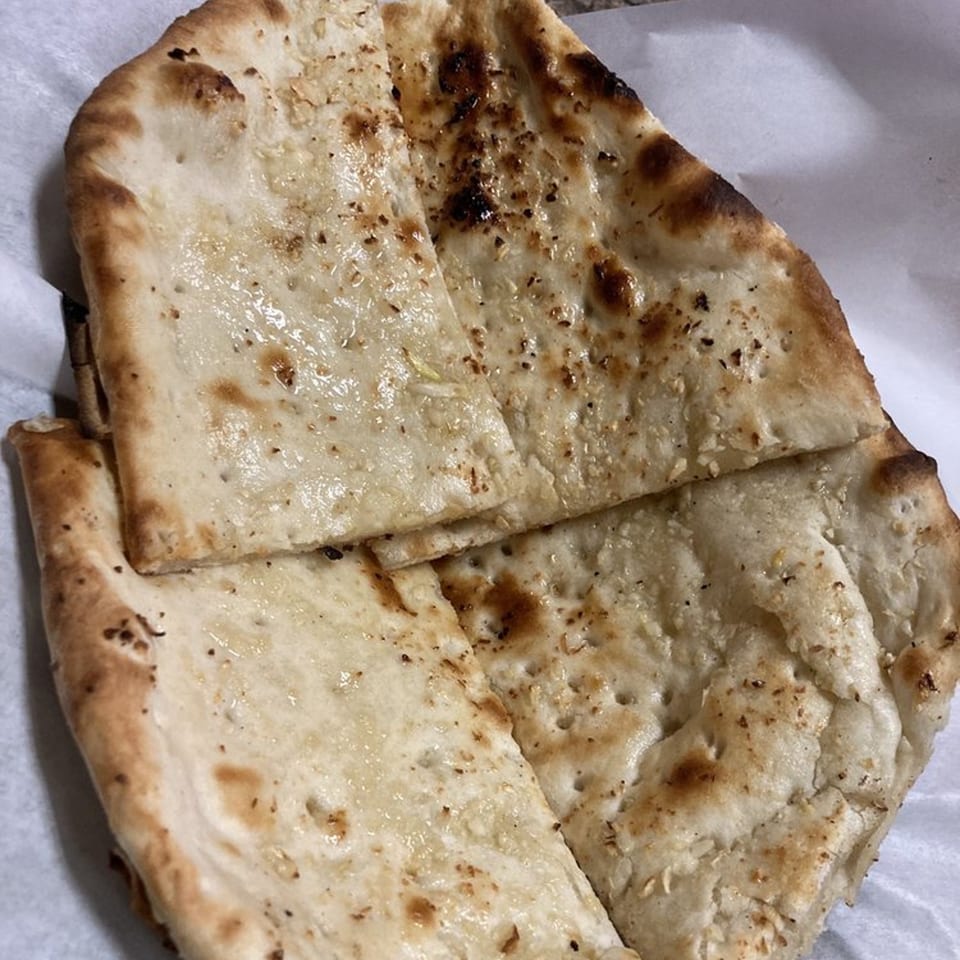 Close-up of several pieces of golden-brown naan bread, lightly charred and sprinkled with herbs.